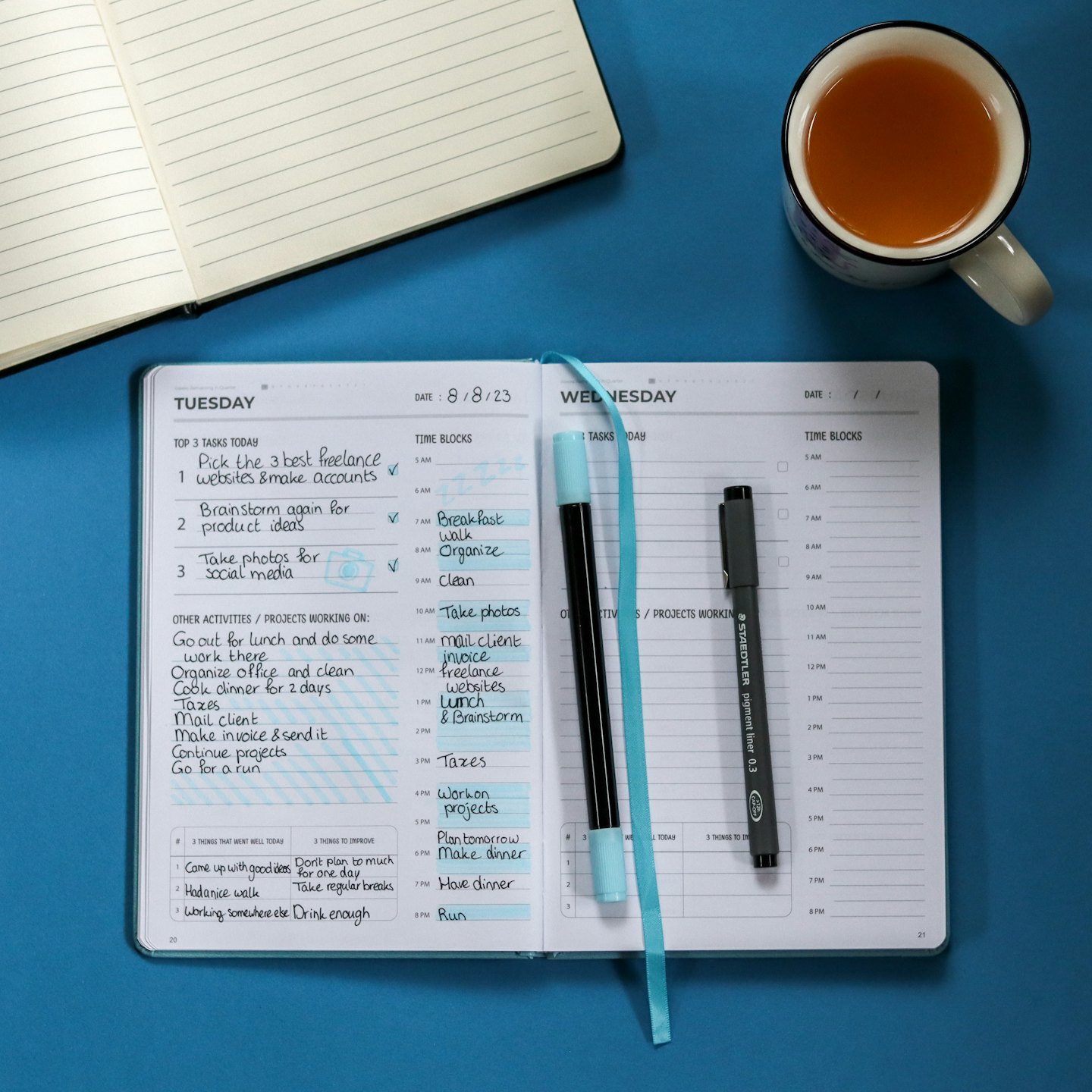 Agenda ouvert avec des tâches manuscrites et des stylos sur fond bleu.